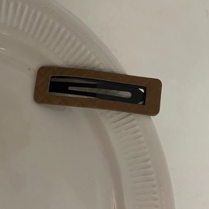 Brown faux leather hair clip with diamond lattice texture on white ceramic plate