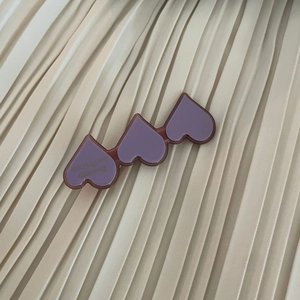 Detail view of purple heart-shaped acetate hair clip with gold lettering on soft fabric