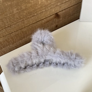 Detailed close-up of a large grey plush faux fur hair claw clip on a clean wooden surface