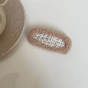 Detail of milk tea color plush hair clip with elegant white and gold tweed fabric inlay