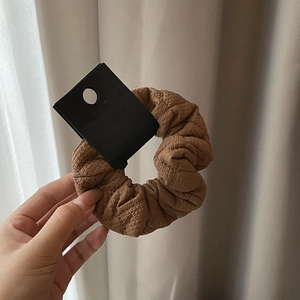 Close-up of brown textured fabric scrunchie with elastic bubble pattern and black card tag