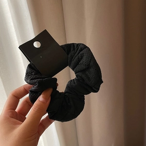French style black scrunchie in textured fabric held by hand with elegant drape