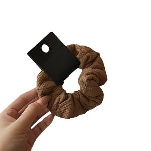 Brown checkered fabric scrunchie with textured surface shown on a display card