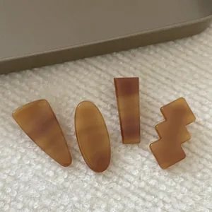 Close-up of four amber acetate hair clips in geometric shapes on soft fabric