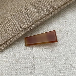 Minimalist amber brown acetate geometric hair clip displayed on textured fabric