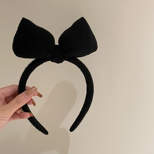 Detail of a black knitted headband with a large bow showing the textured fabric material