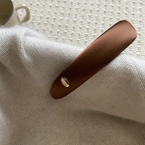 Detail of elegant brown satin hair clip with gold metal tag on white knit fabric