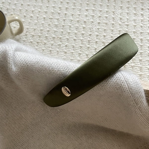 Close-up of olive green satin headband with gold metal plate and Believe In Yourself text