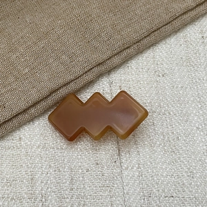 Close-up of amber geometric acetate hair clip on textured beige linen background