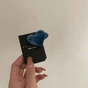 Nahaufnahme einer blauen beflockten Herz-Haarklammer auf Markenkarte vor beigem Hintergrund