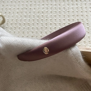 Close-up of padded silk satin headband in dusty pink with a gold engraved metal tag
