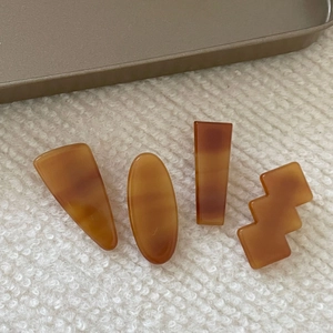 Set of four geometric acetate hair clips with amber texture on white knit fabric