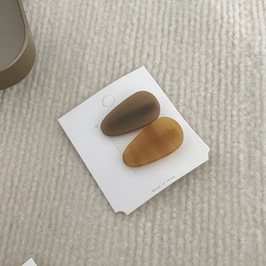 Detail view of two acetate teardrop hair clips in dark brown and amber on display card