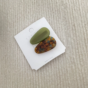 Detail view of two acetate teardrop duckbill hair clips in olive green and tortoiseshell