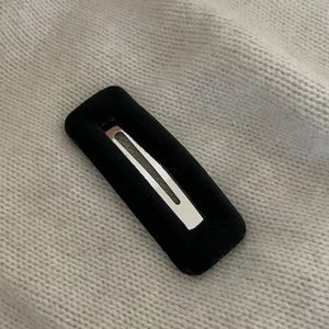 Detailaufnahme einer schwarzen Haarspange mit Samtbezug auf einem gestrickten Hintergrundstoff