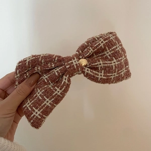 Detailed close-up of brown tweed bow hair clip with engraved gold button accent