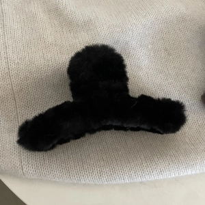 Dettaglio di un mollettone in pelliccia sintetica nera su sfondo in maglia beige
