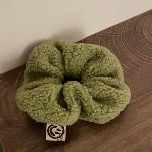 Chouchou en polaire vert olive avec étiquette sourire sur surface en bois