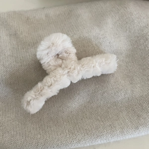 Dettaglio della molletta per capelli in finta pelliccia color crema con trama soffice