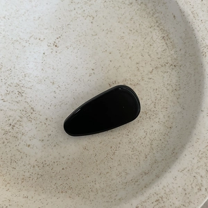 Detail of glossy black water drop hair clip on minimalist white ceramic tray