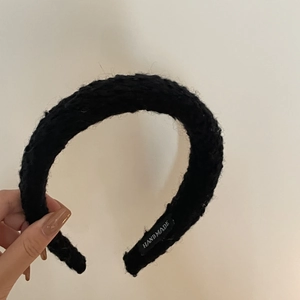 Détail d'un serre-tête large noir fait main montrant la texture en tweed et l'étiquette