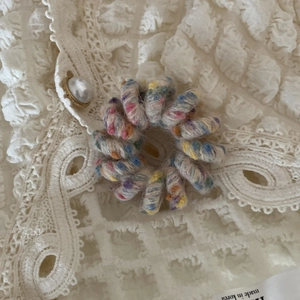 Dettaglio di un elastico per capelli a spirale intrecciato colorato su pizzo bianco