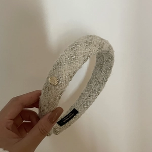 Handmade cream tweed headband with silver thread and a round gold metal plaque charm