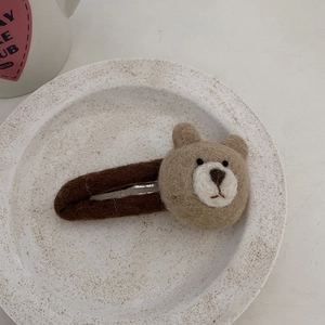 Detail view of a handmade wool felt brown bear hair clip on a white ceramic plate