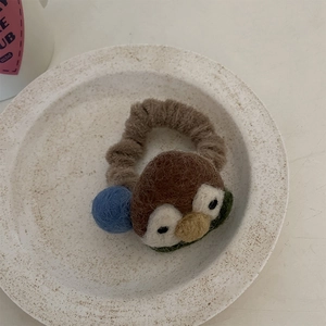 Macro shot of a handmade wool felt penguin hair tie with brown elastic band on stone tray