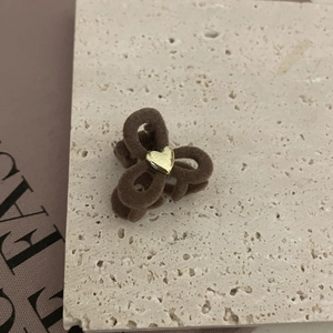 Detalle de una pinza para el pelo flocada marrón con corazón dorado sobre piedra