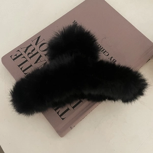 Détail d'une pince à cheveux en peluche noire de 13 cm posée sur un livre lilas