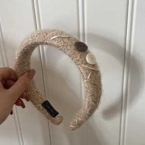 Détail d'un bandeau en maille kaki avec boutons décoratifs et étiquette de fabrication artisanale