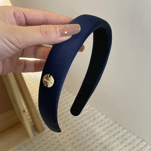 Detail of navy blue padded headband with silky fabric texture and gold metal brand tag