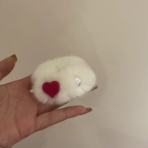 White faux mink fur scrunchie featuring a red heart and pearl accent in a hand-held shot
