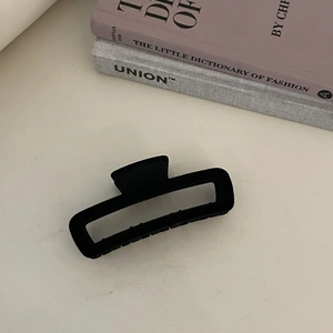 Detail of a large black matte hollow hair claw clip styled on a cream surface
