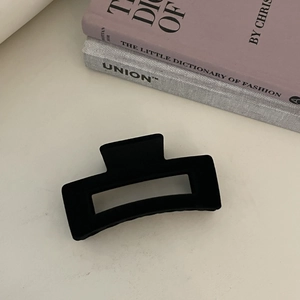 Close-up of a black matte rectangular hair claw clip styled with fashion books