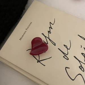 Detail of red heart-shaped acetate hair clip on vintage French book background