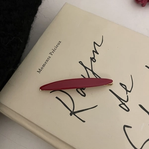 Detail shot of a slim red acetate hair clip on a vintage book cover for hair styling