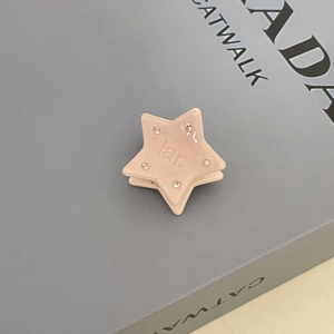 Pink acetate star hair claw clip with rhinestones on a stylish book background
