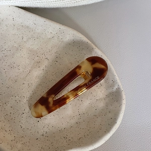 Minimalist tortoiseshell acetate hair clip with oval cutout on a ceramic plate