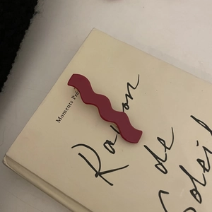 Detail view of a wavy burgundy acetate hair clip on an artistic decorative card