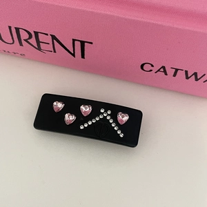 Detail view of black rectangular hair clip with pink heart rhinestones and CD logo