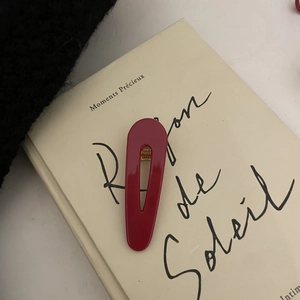 Red acetate hollow hair clip on book background, stylish minimalist hair accessory