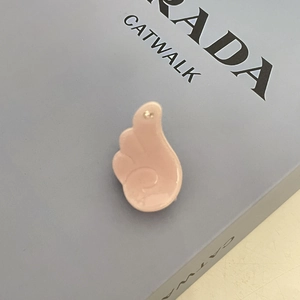 Close-up of a pink glossy wing-shaped hair clip pendant resting on a fashion book