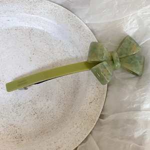 Detail of green bow acetate hair clip with marble texture on minimalist tray