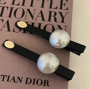 Paire de pinces à cheveux noires mates avec perle et plaque dorée sur fond rose