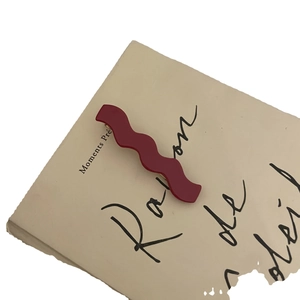 Elegant wave-shaped burgundy acetate hair clip on vintage paper with gold metal base