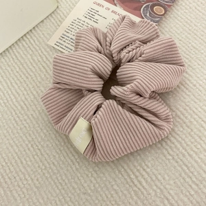 Pink corduroy scrunchie with Korea woven label on plush white background