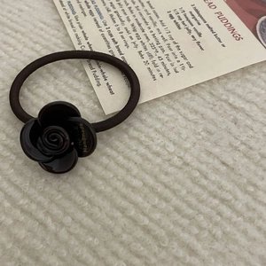 Close-up of brown resin camellia hair tie with gold handmade lettering on knit background