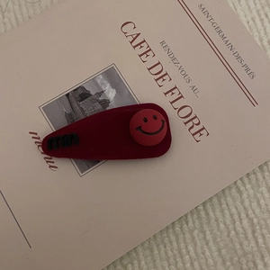 Dettaglio della molletta per capelli in velluto rosso con bottone smiley e ricamo nero